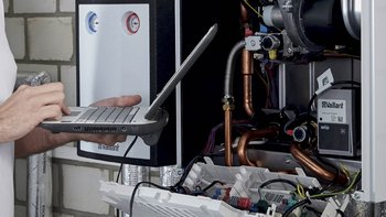 Ein Techniker arbeitet an einer Heizungsanlage, während er ein Laptop zur Diagnose verwendet, um Einstellungen zu überprüfen.