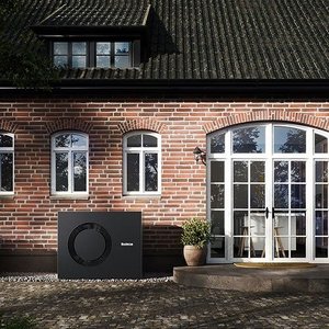 Ein modernes Heizgerät steht neben einem charmanten Backsteinhaus mit großen Fenstern und einer eleganten Glastür.