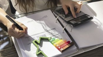 Eine Person schreibt mit einem Stift auf einem Dokument, während sie einen Taschenrechner benutzt und eine grüne Wachstumsmarkierung betrachtet.