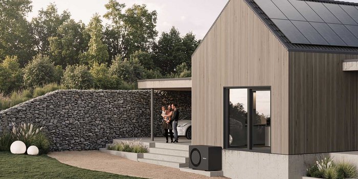 Eine Familie steht auf der Terrasse eines modernen Hauses mit Holzverkleidung und begrüßt den Sonnenuntergang.